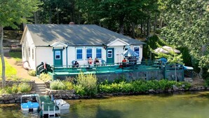 A lakeside cabin with a dock, a covered deck, and a small boat. - Waterfront Lake House Cottage Private Dock, Deck, Kayak, Boat, Swim, Fish, RELAX (Deerfield)