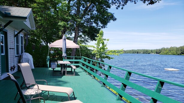 A deck with green railings overlooking a lake, featuring outdoor seating and a covered table. - Waterfront Lake House Cottage Private Dock, Deck, Kayak, Boat, Swim, Fish, RELAX (Deerfield)