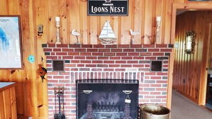 A fireplace with a brick surround, a sign above it reading "Loons Nest," and a map on the wall to the left. - Waterfront Lake House Cottage Private Dock, Deck, Kayak, Boat, Swim, Fish, RELAX (Deerfield)