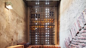 A narrow room with a brick wall, a wooden bench, and a metal rack with bottles.
