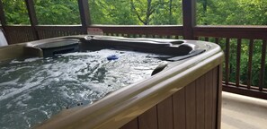 Relax in the hot tub on the deck surrounded by lush greenery.