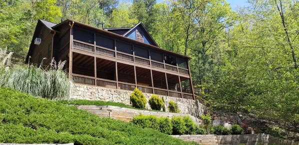 Escape to a serene forest retreat with a two-story cabin featuring a spacious balcony and a view of the surrounding trees.