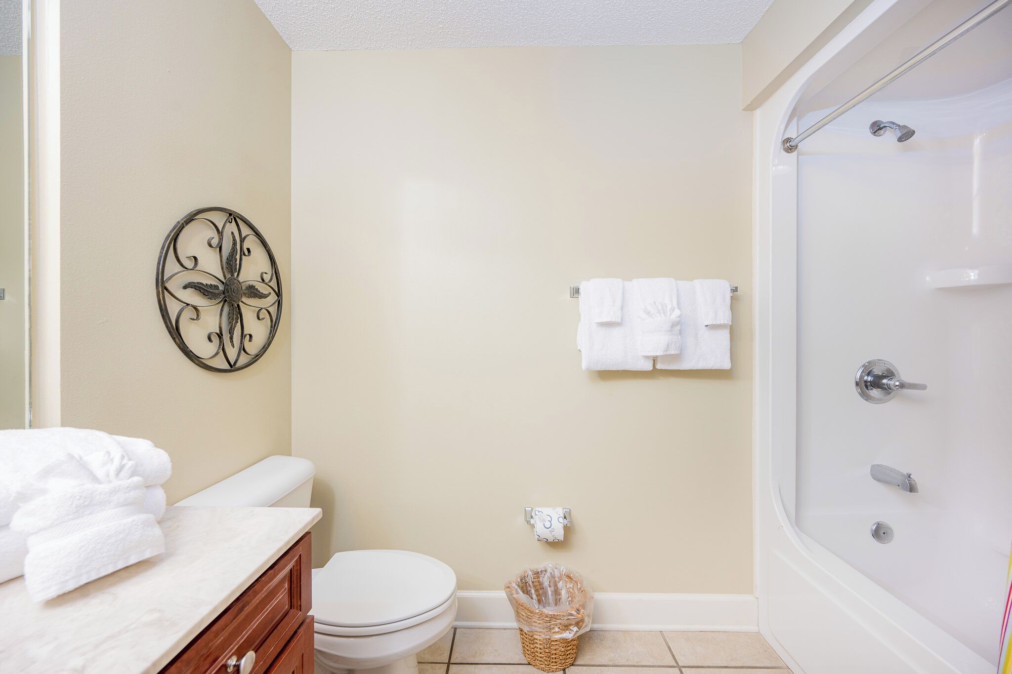 A bathroom with a toilet, a sink with a towel, a shower, and a decorative wall piece.