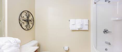 A bathroom with a toilet, a sink with a towel, a shower, and a decorative wall piece.