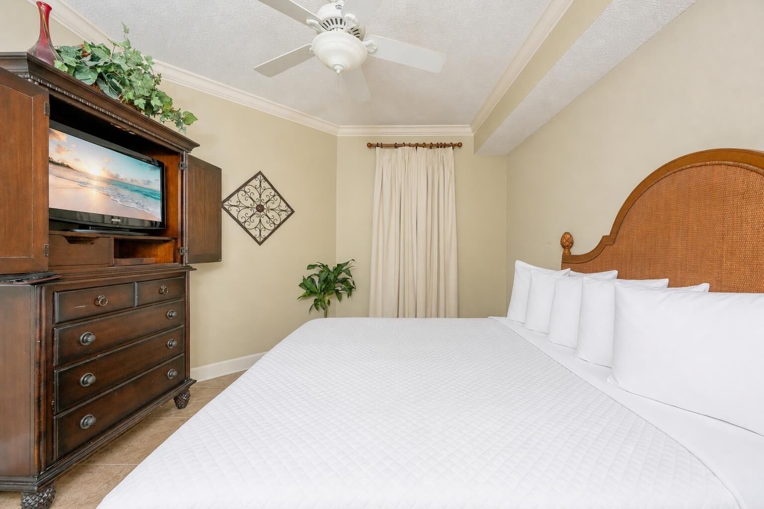 Een hotelkamer met een groot bed, een houten dressoir, een plafondventilator, een televisie en een decoratief wandobject.