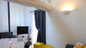 Ein Wohnzimmer mit einer Couch, einem kleinen Tisch, einem Fernseher und einem Fenster mit Vorhängen.