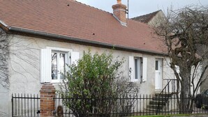 Ein zweigeschossiges Haus mit rotem Ziegeldach, weißen Fensterrahmen und einem Backsteinsschornstein.