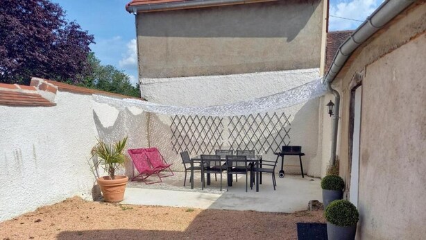 Eine Terrasse mit Tisch, Stühlen, einem Grill und Kübelpflanzen.