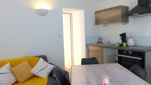 Ein gemütlicher Wohnbereich mit Esstisch, einer Couch mit Kissen, einer Küchenzeile und einer Wandleuchte.