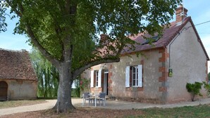 Una casa rústica con fachada de ladrillo, techo de tejas y un gran árbol en la entrada.