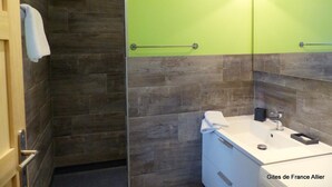 Un baño con piso de madera, pared verde, lavamanos blanco y una toalla colgada en la puerta.