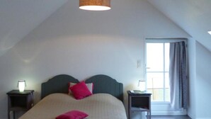 Un dormitorio con techo inclinado, una cama con cabecera, dos mesitas de noche con lámparas y una ventana con cortinas.