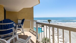 A balcony with blue and white Adirondack chairs, a pool, and a view of the beach and ocean.