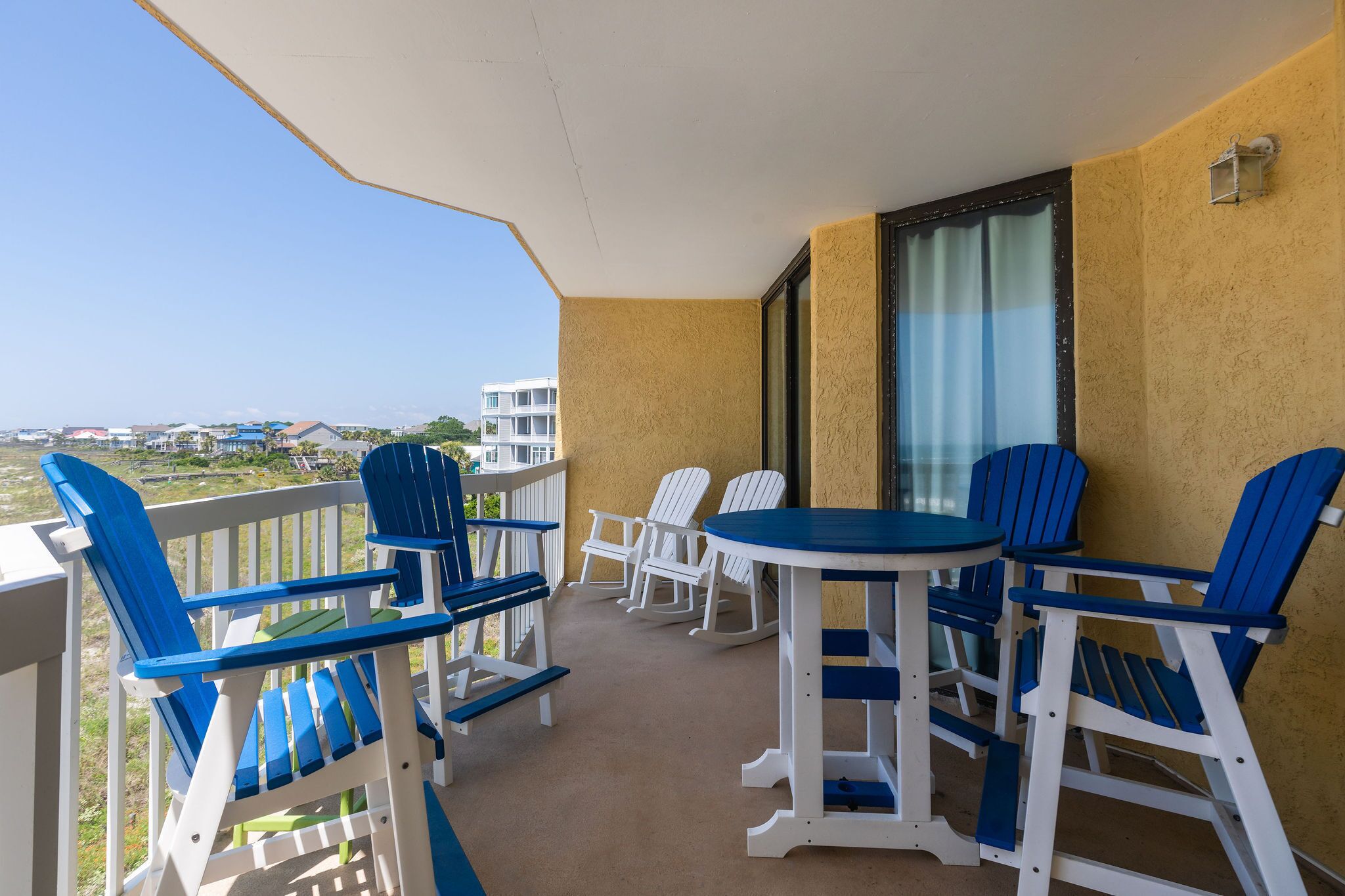Un balcón con sillones Adirondack azules y blancos y una pequeña mesa, con vistas a un paisaje urbano.