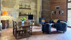 A rustic living room with exposed stone walls, a wooden ceiling, a dining table with chairs, a sofa, a fireplace, and a television. - Restored Shepherd's Hut, Pets Allowed (Sauvagny)
