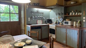 A compact kitchen with a central island, a dining table with a covered area, and a window with a view of greenery. - Restored Shepherd's Hut, Pets Allowed (Sauvagny)