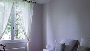 Une chambre à coucher avec un lit, une table de chevet, une chaise et une fenêtre avec des rideaux.