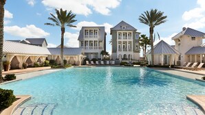 A pool area with a large building in the background, palm trees, and lounge chairs. - Huge Ocean View - Spa/Pool/Golf Cart (Port Aransas)