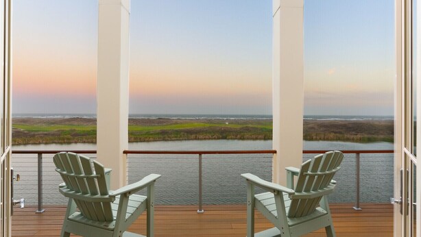 A balcony with two Adirondack chairs overlooking a body of water and a coastal landscape. - Huge Ocean View - Spa/Pool/Golf Cart (Port Aransas)