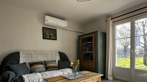 A living room with a sofa, a wooden coffee table, a cabinet, and a large window. - Country house, AC - 4 guests (Saint-Bonnet-Tronçais)