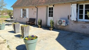 A building with a tiled roof, a bench, a table with chairs, and a potted plant. - Country house, AC - 4 guests (Saint-Bonnet-Tronçais)