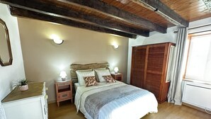 A bedroom with a wooden ceiling, a bed with white bedding, a nightstand with a lamp, a wardrobe, and a window with curtains. - Country house, AC - 4 guests (Saint-Bonnet-Tronçais)
