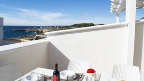 A balcony with a table set for dining, overlooking a coastal landscape with buildings and cliffs.
