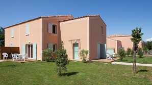 Un edificio de dos pisos con techo plano, un patio cubierto con mesas al aire libre y un césped bien cuidado.