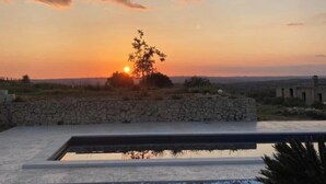 A sunset view over a swimming pool with a stone wall and a tree in the foreground.