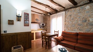 Une pièce chaleureuse avec un mur en pierre, des meubles en bois, un coin repas et une fenêtre avec des rideaux.