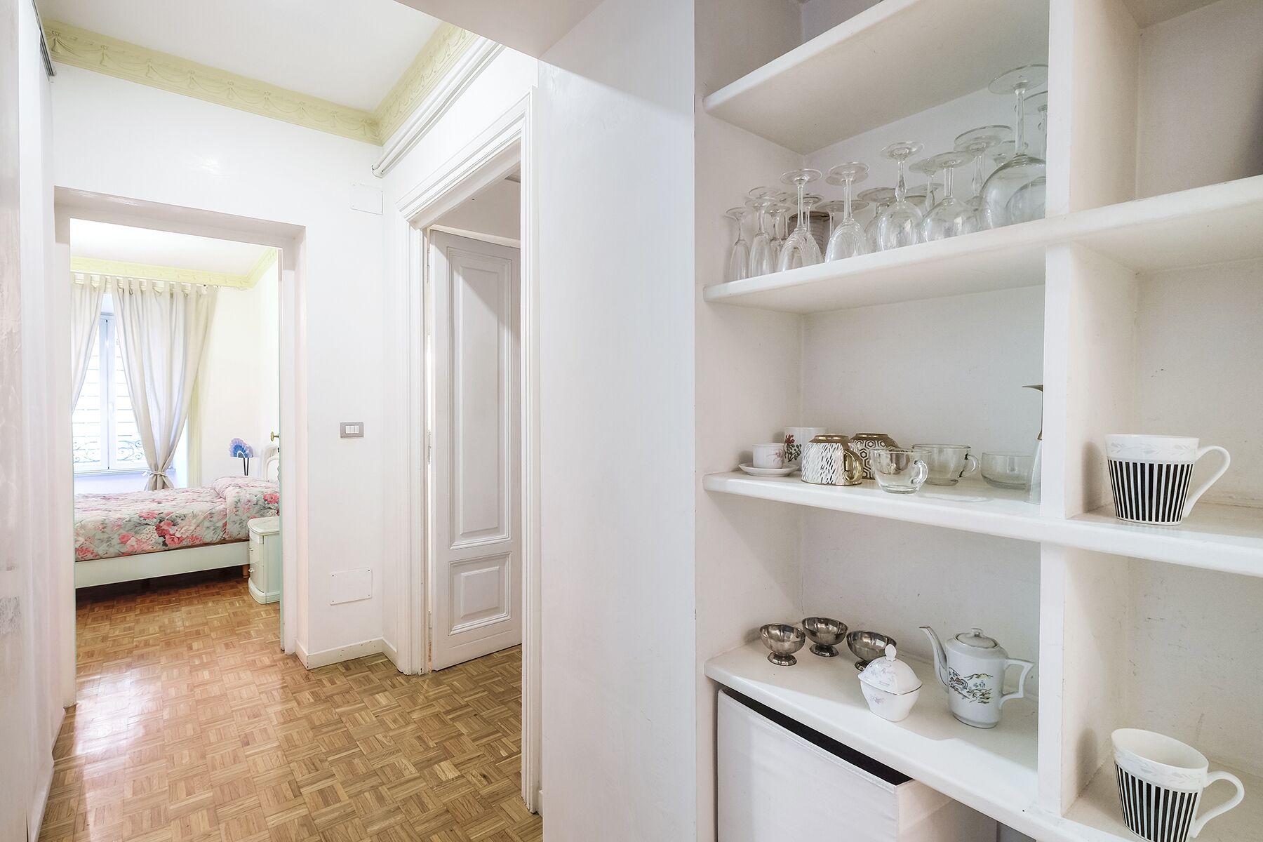 Une pièce avec un plancher en bois, un lit recouvert d’une literie à motifs floraux et une porte blanche.