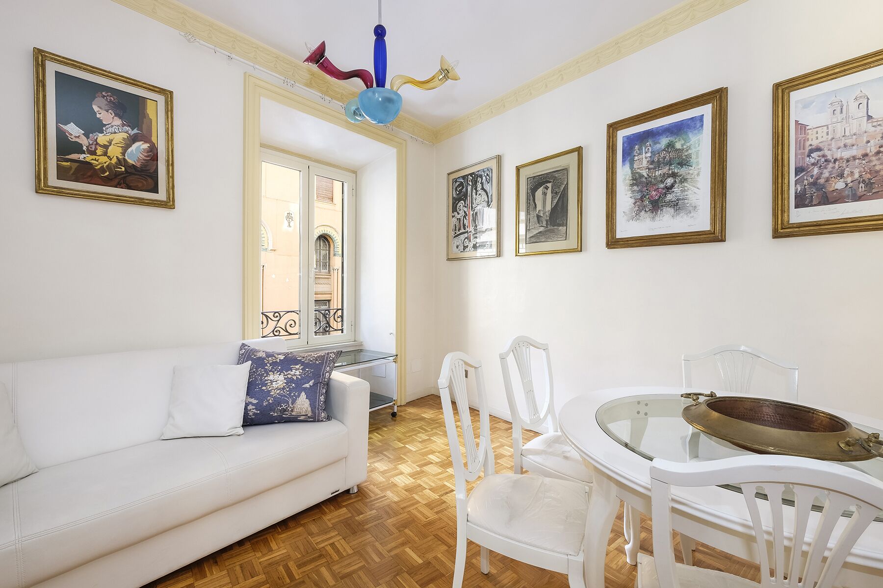 A room with a white sofa, a dining table with chairs, and several framed artworks on the walls.