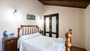 A bedroom with a wooden bed, a nightstand, a dresser, and a door with frosted glass panels. - Casa del Agüelo: Apartment Teruel (5 people) (Cella)