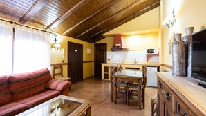 A cozy living room with a sofa, a glass coffee table, and a wooden dining table with chairs. There's a kitchen area with a microwave, a red stove, and wicker baskets. - Casa del Agüelo: Apartment Teruel (5 people) (Cella)