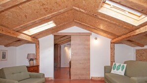 A cozy loft-style room with wooden beams, a high ceiling, and a skylight. There are two green sofas and a striped rug on the wooden floor. - Tre Rose by Interhome (Opatija/Zvoneće)