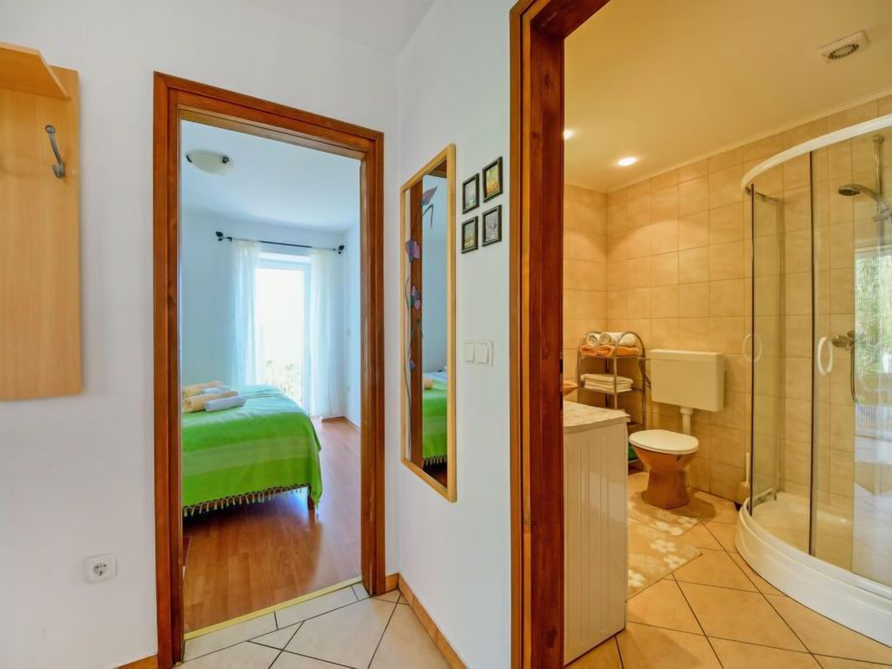 Een hotelkamer met een bed, een badkamer met toilet en douche, en een gang naar een andere kamer.