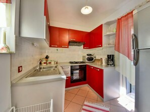 A compact kitchen with red cabinets, a microwave, a stove, and a refrigerator. - Vacation home Bruna by Interhome (Brsec)