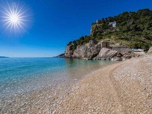 A pebble beach with clear water, a rocky cliff, and a building on top. - Vacation home Bruna by Interhome (Brsec)