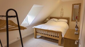 A bedroom with a sloped ceiling, a wooden bed, a bedside table, a mirror, and a hanging dreamcatcher.