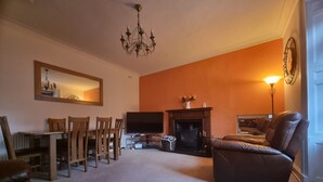 A living room with a fireplace, a television, a dining area with chairs, and a sofa.