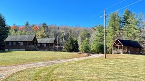 A rustic cabin with a porch, surrounded by a grassy field and trees.