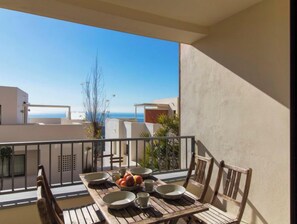 A balcony with a table set for dining, overlooking a coastal view.