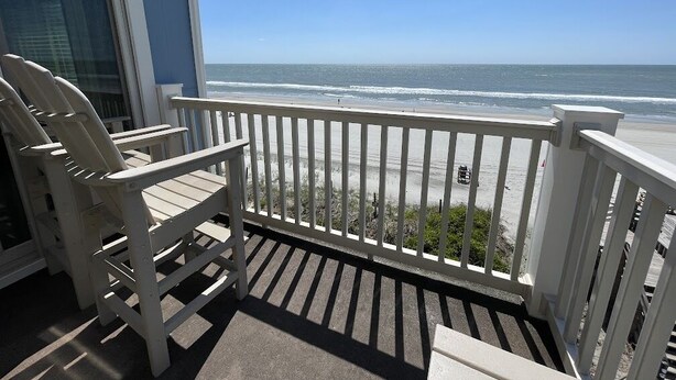 Un balcon avec des balustrades blanches donnant sur une plage.