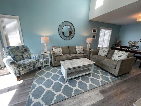 A living room with a light blue wall, two sofas, a coffee table, and a patterned rug.