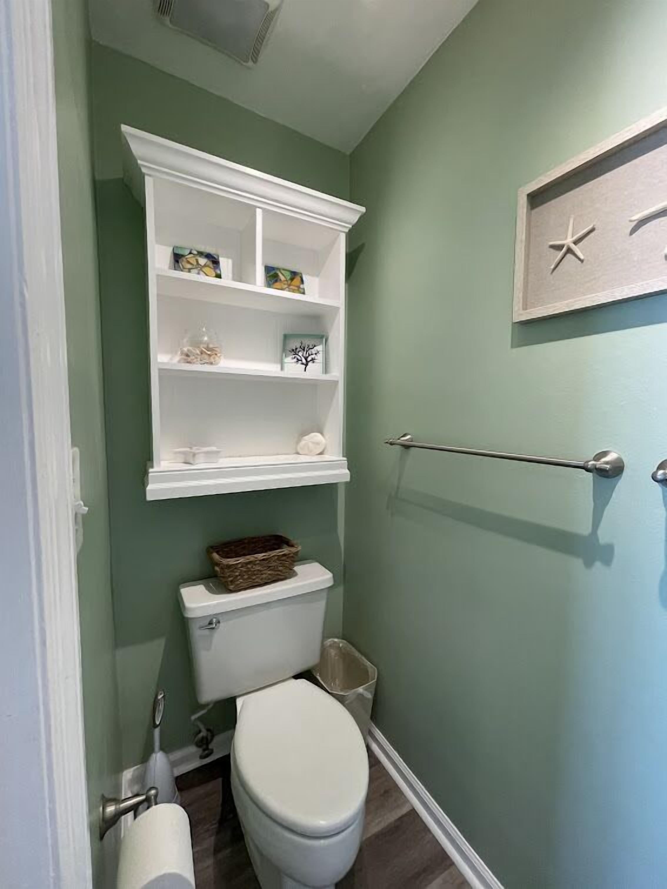 Un baño con inodoro, una estantería con objetos decorativos, un perchero y una decoración de estrella de mar montada en la pared.