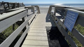 Une promenade en bois mène à une plage où un panneau invite les visiteurs à se débarrasser du sable.