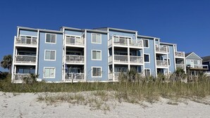 Un immeuble à plusieurs étages situé en bord de mer, doté de balcons, qui est probablement un hôtel ou un ensemble d’appartements.