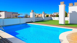 A swimming pool with a wooden deck, surrounded by white walls and a clear blue sky.
