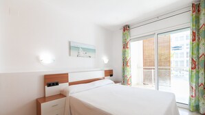 A bedroom with a bed, a nightstand, a wall-mounted light, a window with a view, and a painting on the wall.