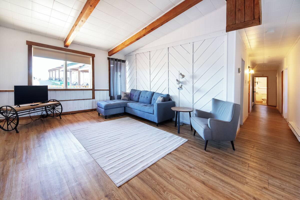 A modern living room with a sectional sofa, a small round table, a television, and a large window.